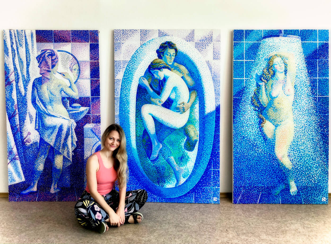 Kristina Korò sitting in front of her triptych showing "the youth" "fusion" and "fruit of love". The 3 pieces show the armony for classical plastic and patterns of blue, white and iris violet.